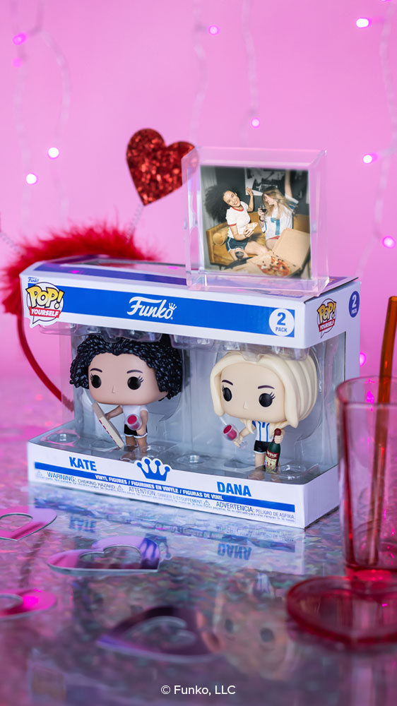 This photo shows a 2-pack POP! Yourself box with the names Kate and Dana written on them. Two POP! Yourself female figures are inside, and they're holding wine glass accessories. Above them, there's a photo of the real-life people they represent. Glittery hearts appear on the wall behind them.